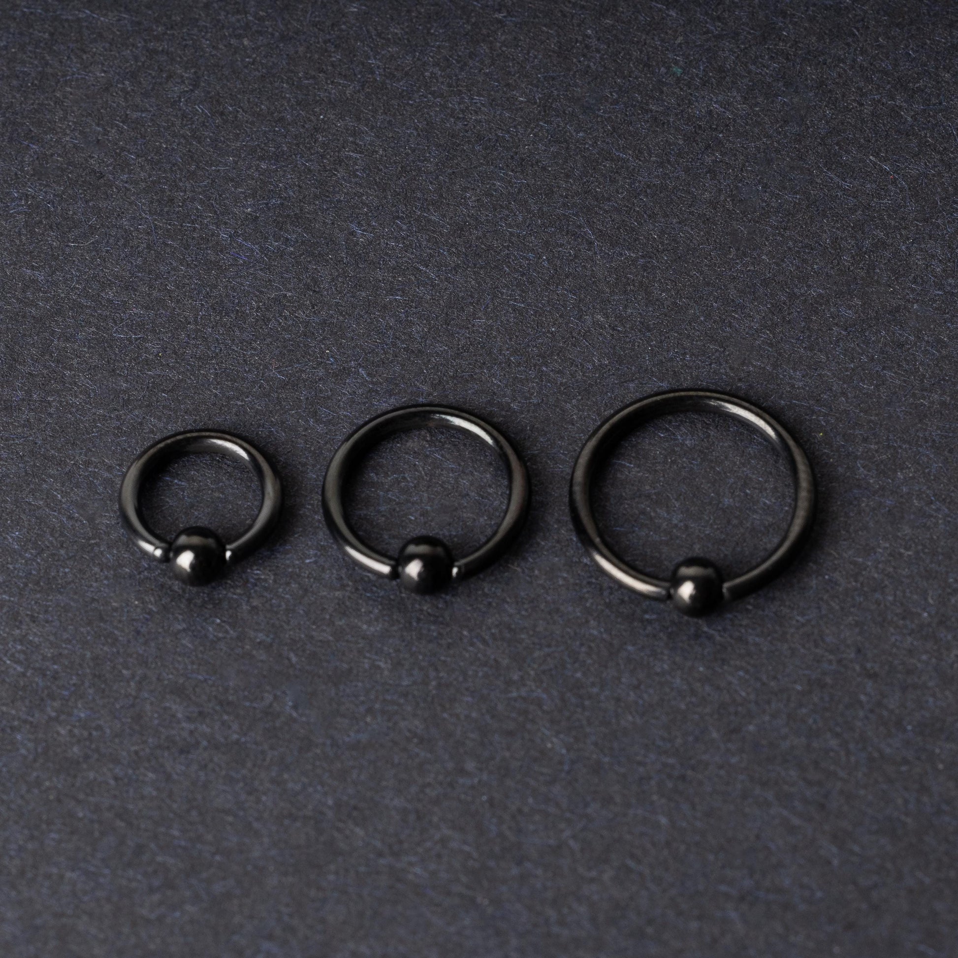 Three black ball closure rings (BCR) in varying sizes, displayed on a dark background with a polished finish and secure captive balls.