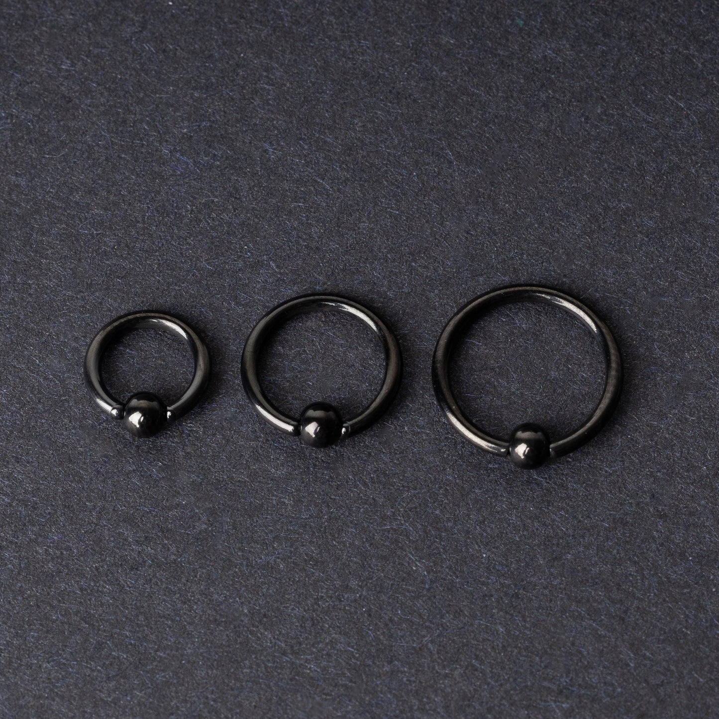 Three black ball closure rings (BCR) in varying sizes, displayed on a dark background with a polished finish and secure captive balls.