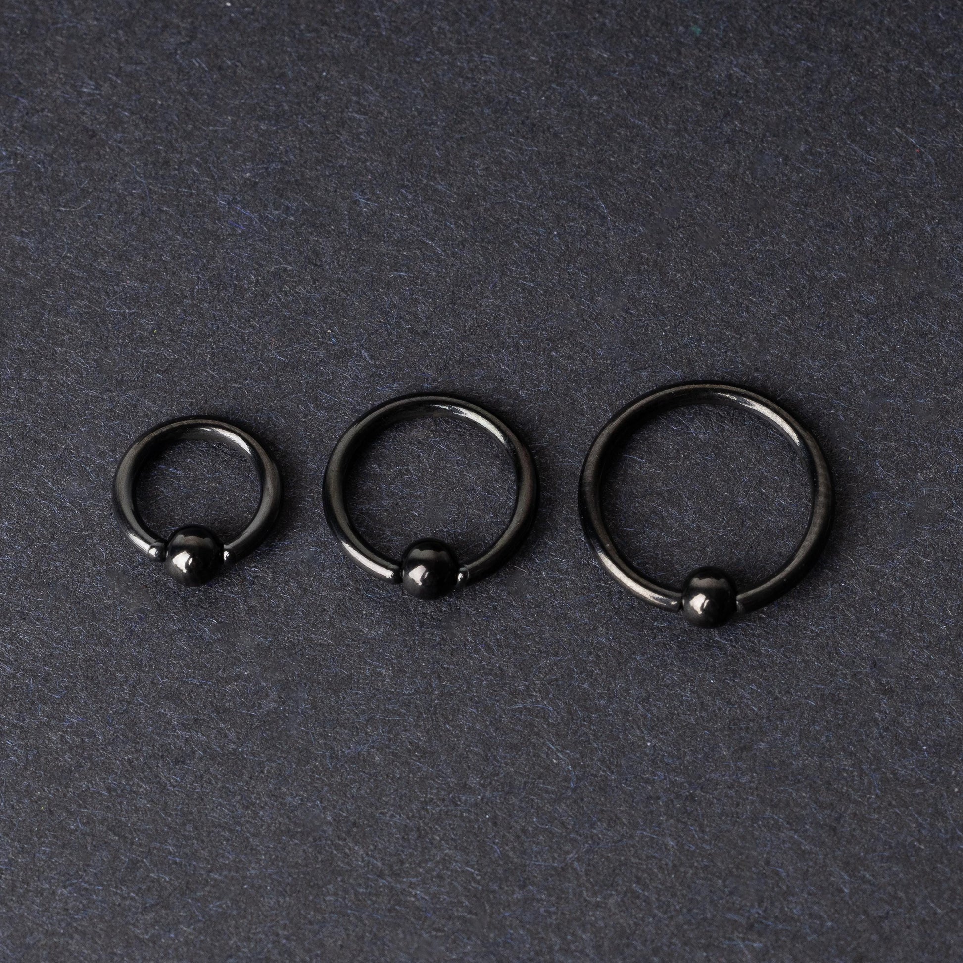 Three black ball closure rings (BCR) in varying sizes, displayed on a dark background with a polished finish and secure captive balls.