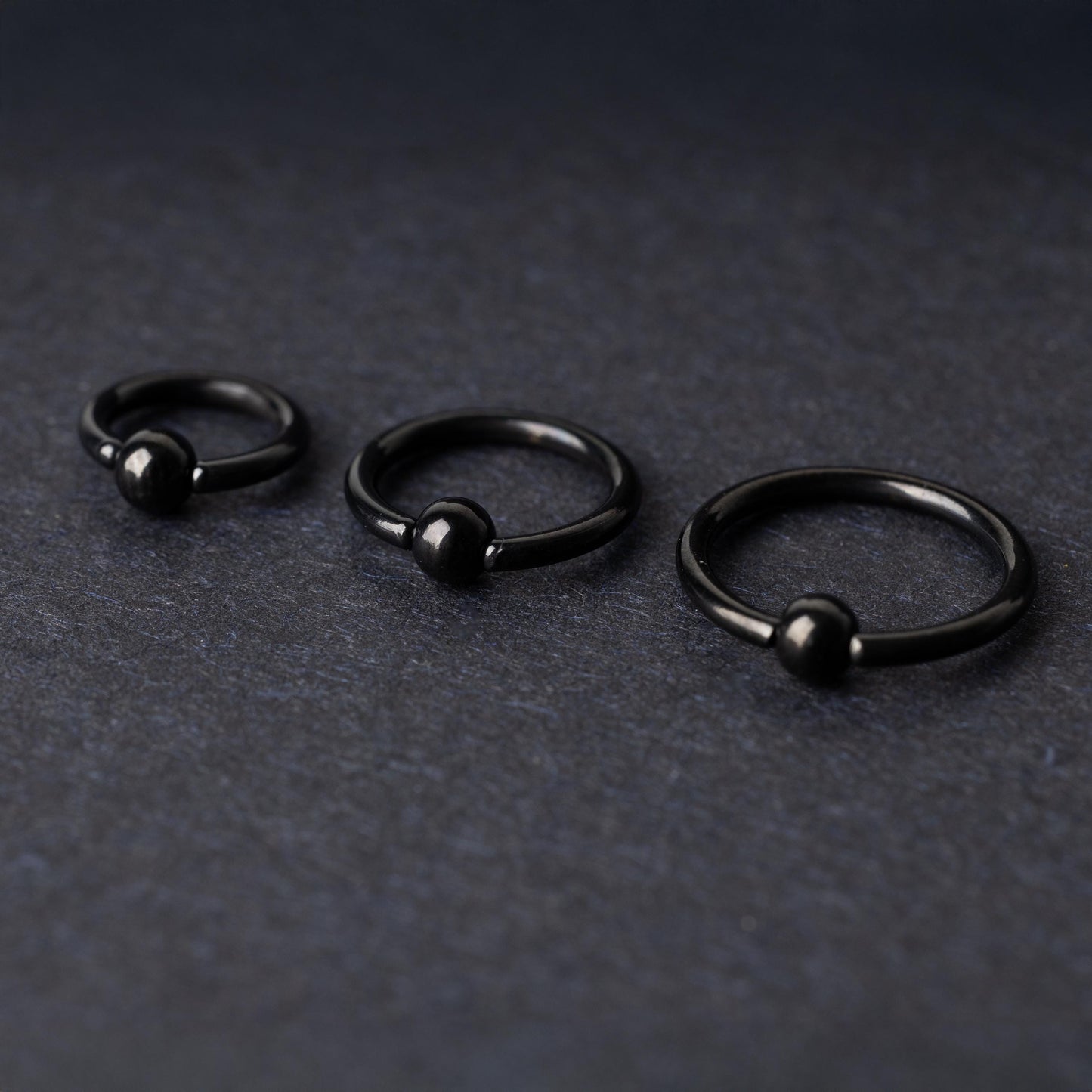 Three black ball closure rings (BCR) in varying sizes, displayed on a dark background with a polished finish and secure captive balls.