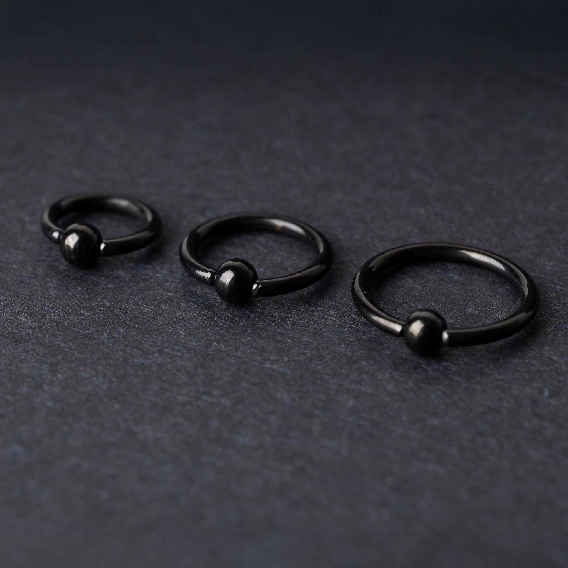 Three black ball closure rings (BCR) in varying sizes, displayed on a dark background with a polished finish and secure captive balls.