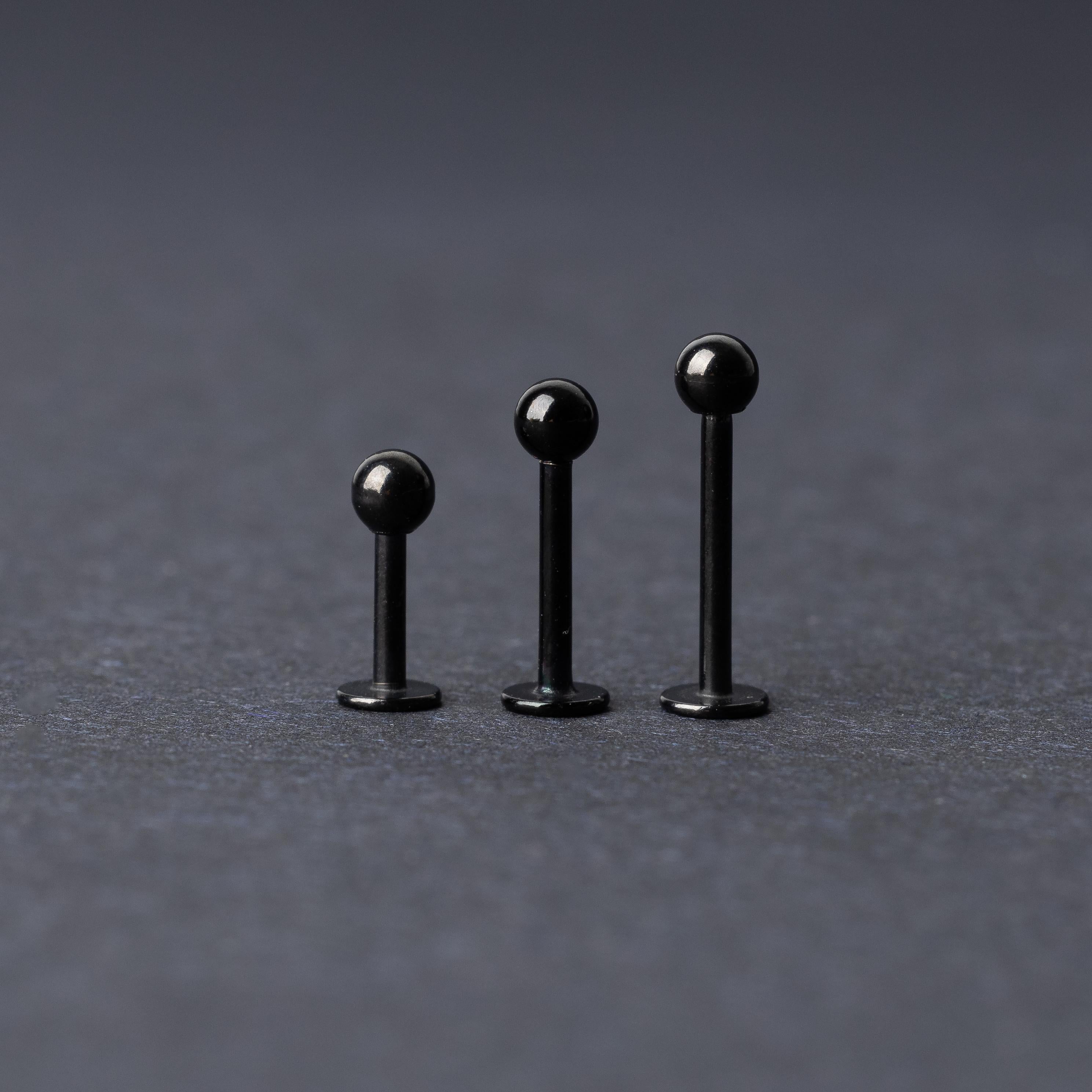 Three black stainless steel flat back barbells with polished finishes, displayed on a dark background.