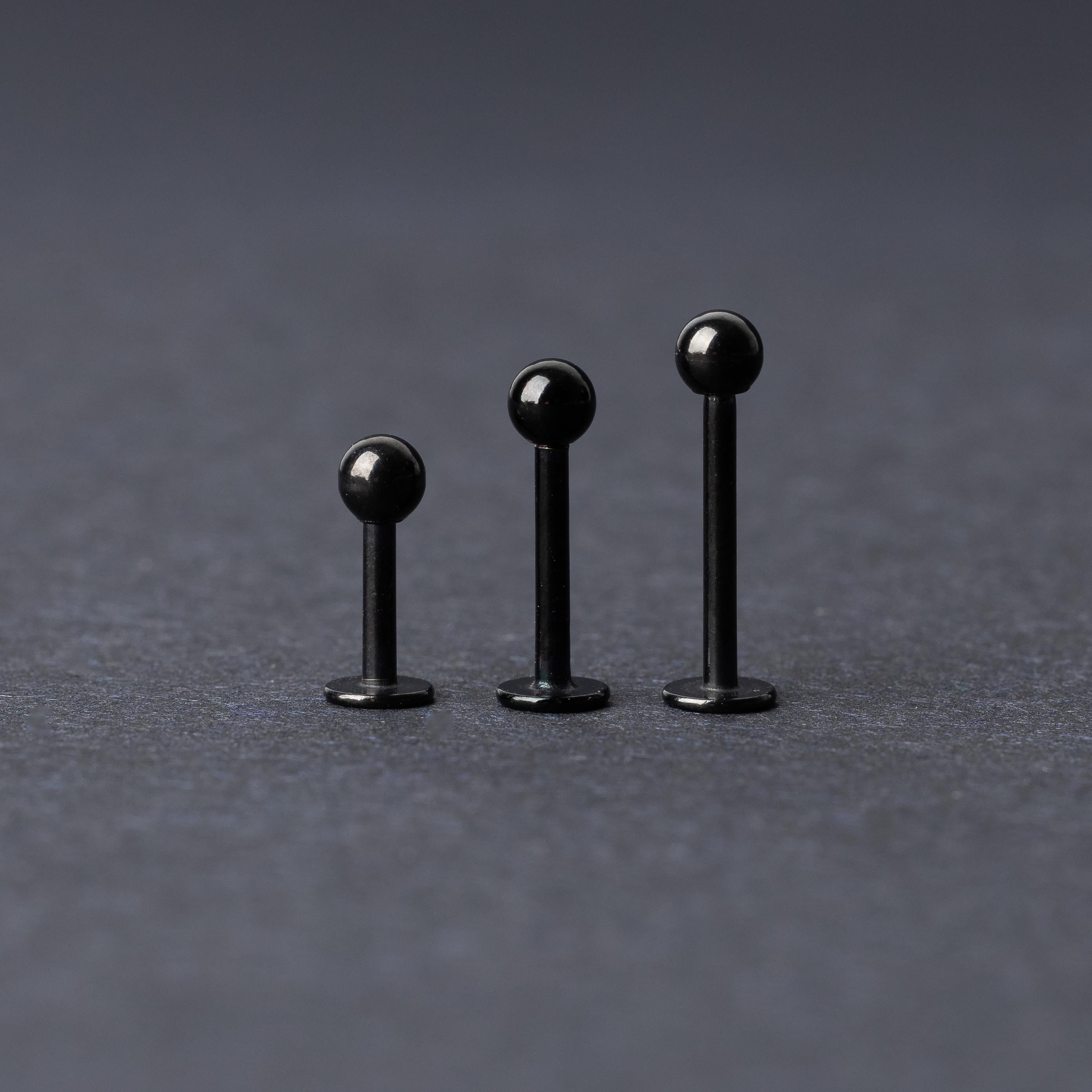 Three black stainless steel flat back barbells with polished finishes, displayed on a dark background.