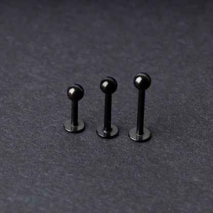 Three black stainless steel flat back barbells with polished finishes, displayed on a dark background.