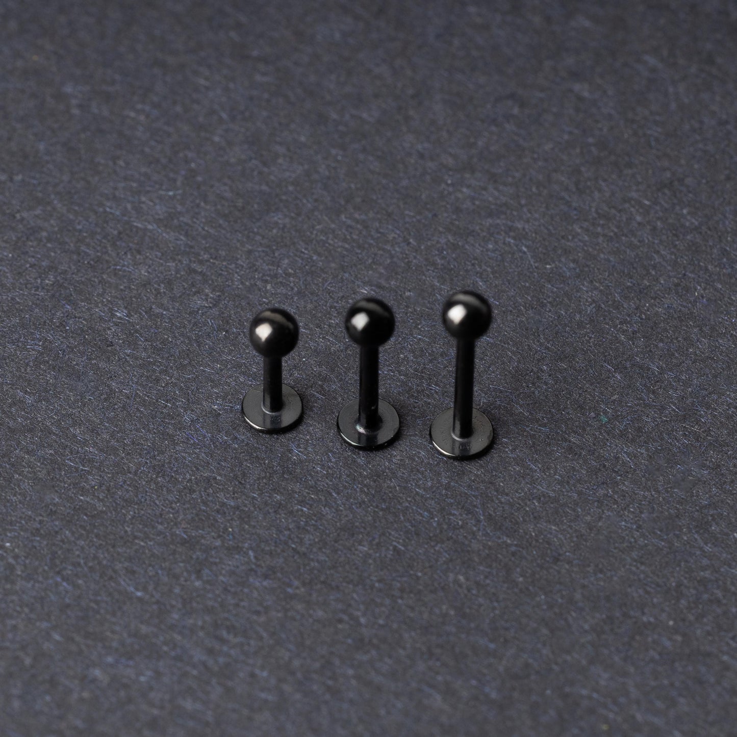 Three black stainless steel flat back barbells with polished finishes, displayed on a dark background.