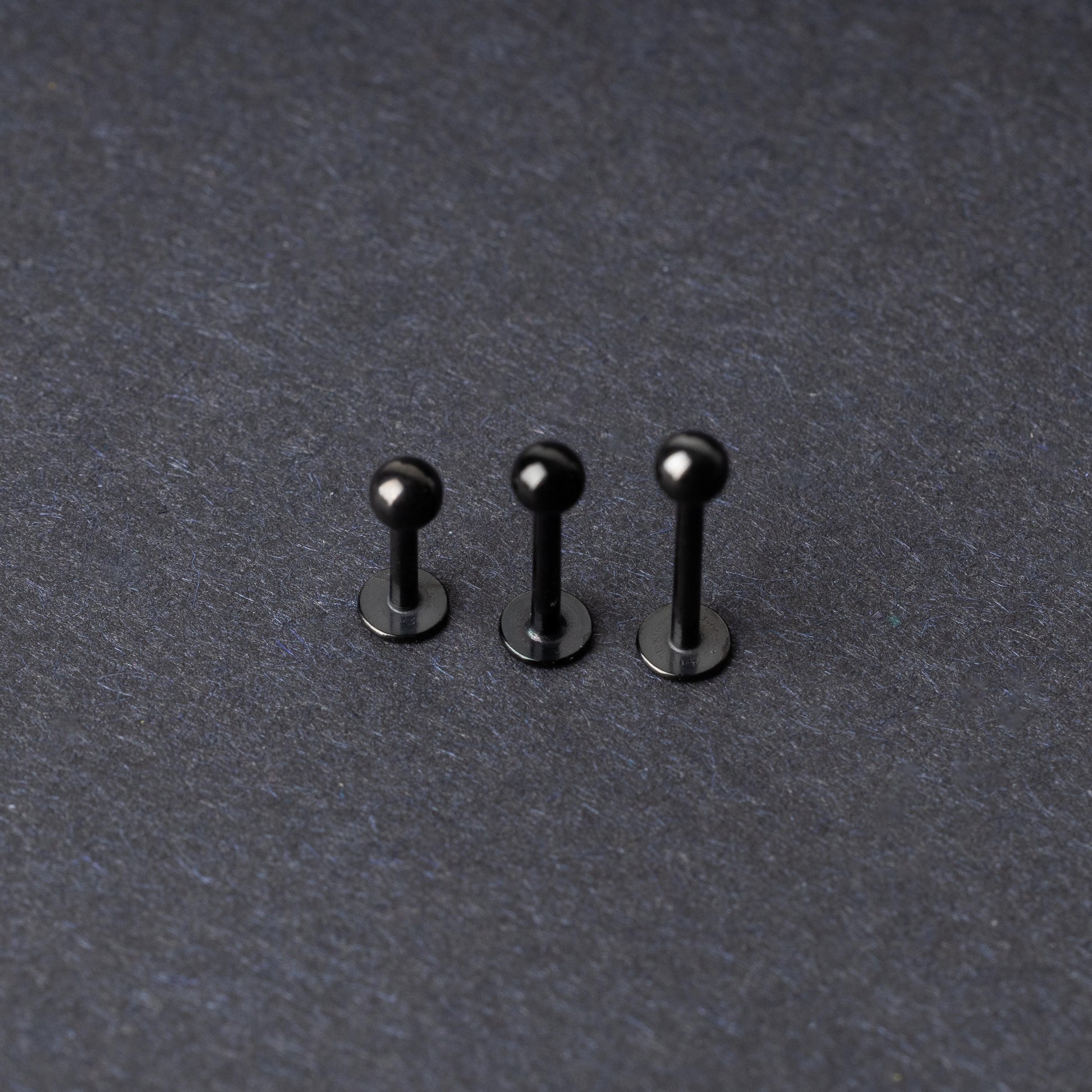 Three black stainless steel flat back barbells with polished finishes, displayed on a dark background.