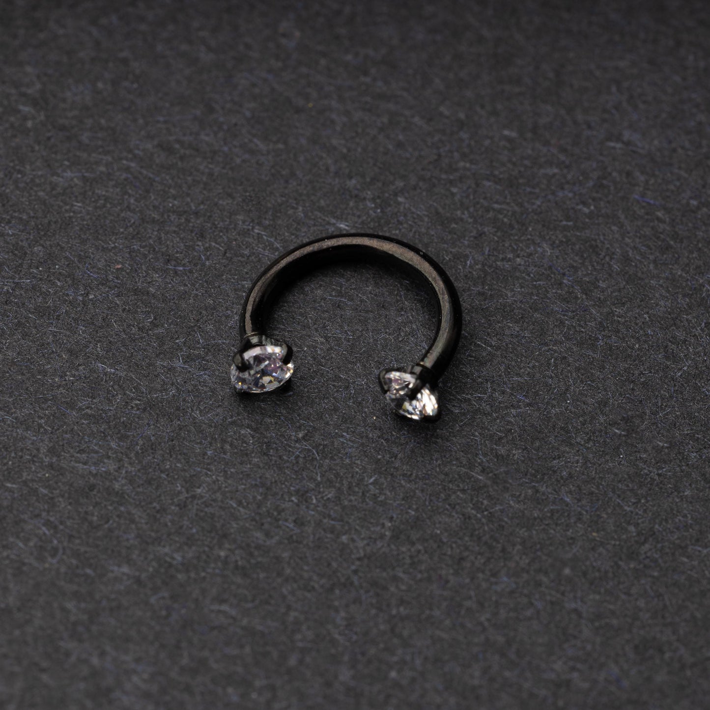 A black jewelled horseshoe hoop with gemstone ends, displayed on a dark background.