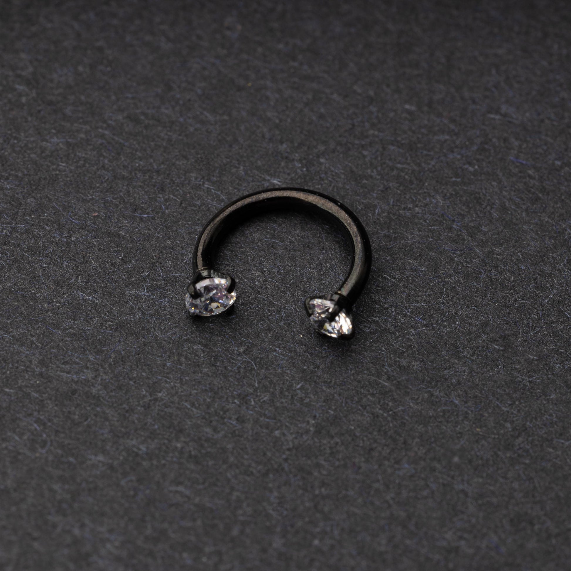 A black jewelled horseshoe hoop with gemstone ends, displayed on a dark background.