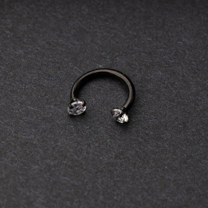 A black jewelled horseshoe hoop with gemstone ends, displayed on a dark background.