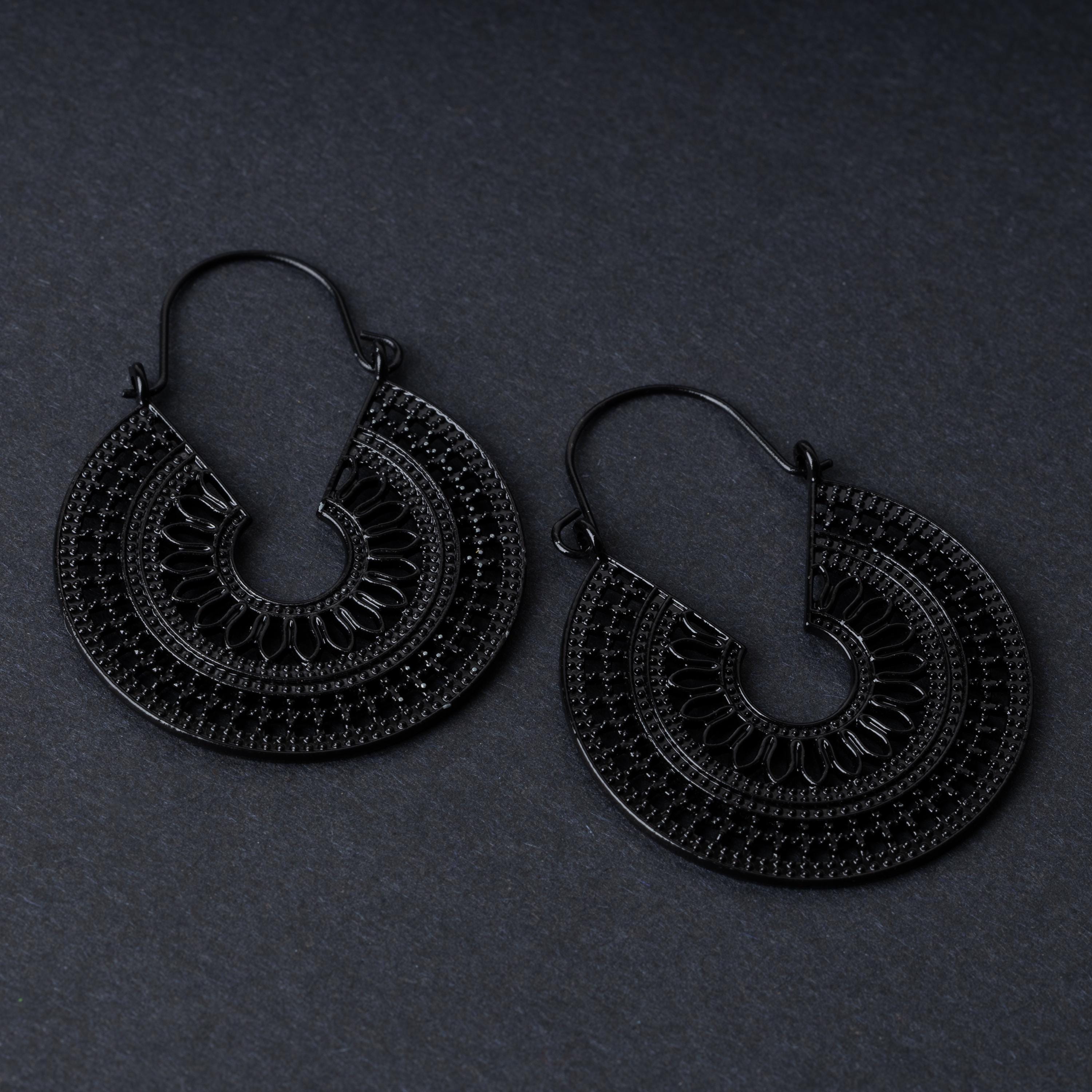 Pair of black hoop earrings with intricate cutout details and textured patterns, displayed on a dark background.
