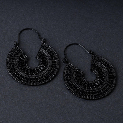 Pair of black hoop earrings with intricate cutout details and textured patterns, displayed on a dark background.