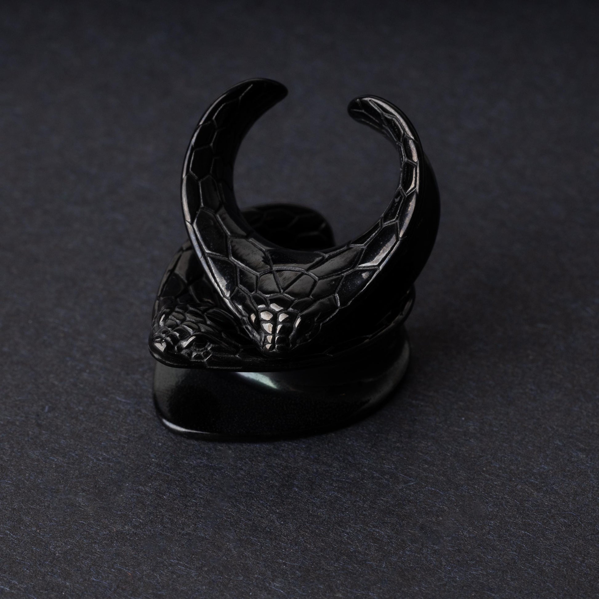 A pair of snakehead saddle tunnels for stretched ears in black, displayed on a dark background.