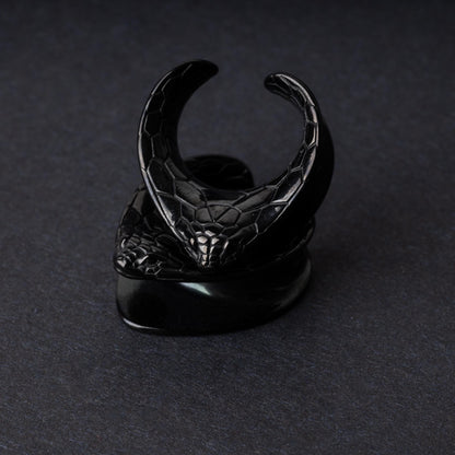 A pair of snakehead saddle tunnels for stretched ears in black, displayed on a dark background.