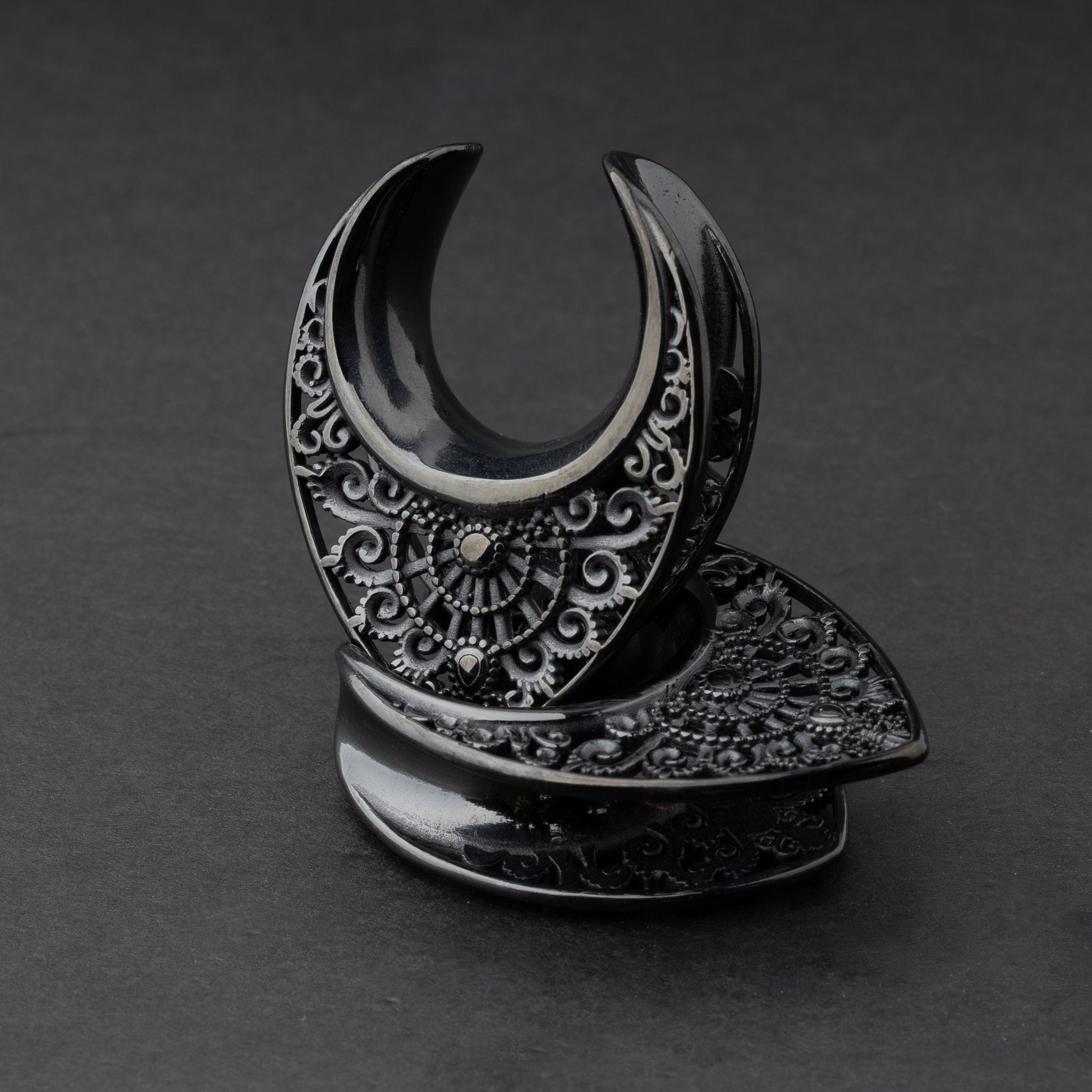 Crescent moon plugs for stretched ears in black, displayed against a dark background.