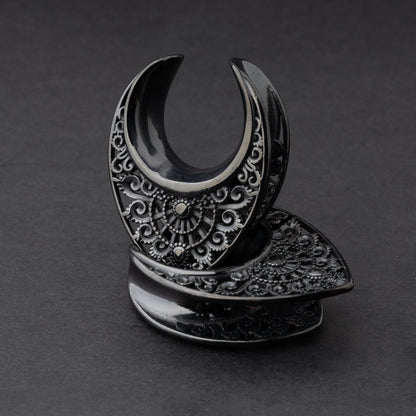 Crescent moon plugs for stretched ears in black, displayed against a dark background.