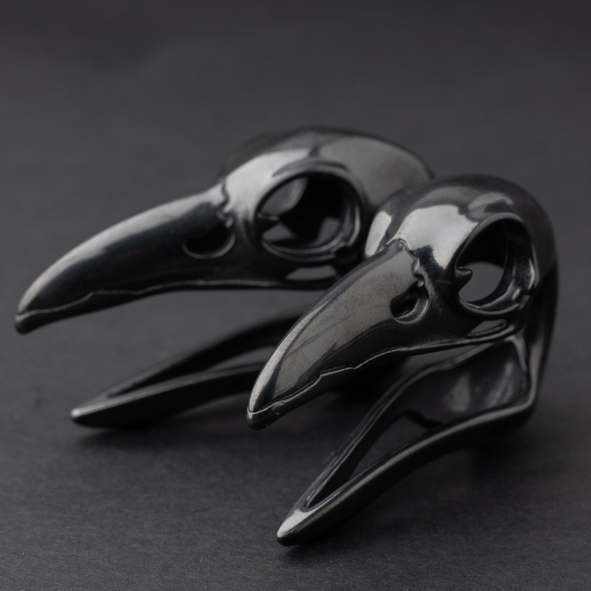 Raven skull saddle plugs in black, elegantly displayed on a dark background.