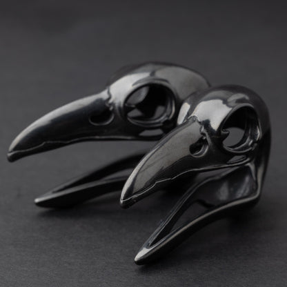 Raven skull saddle plugs in black, elegantly displayed on a dark background.