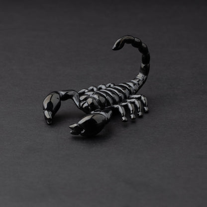 Scorpion-shaped ear hanger in black displayed on a dark matte background, highlighting their detailed and edgy design.