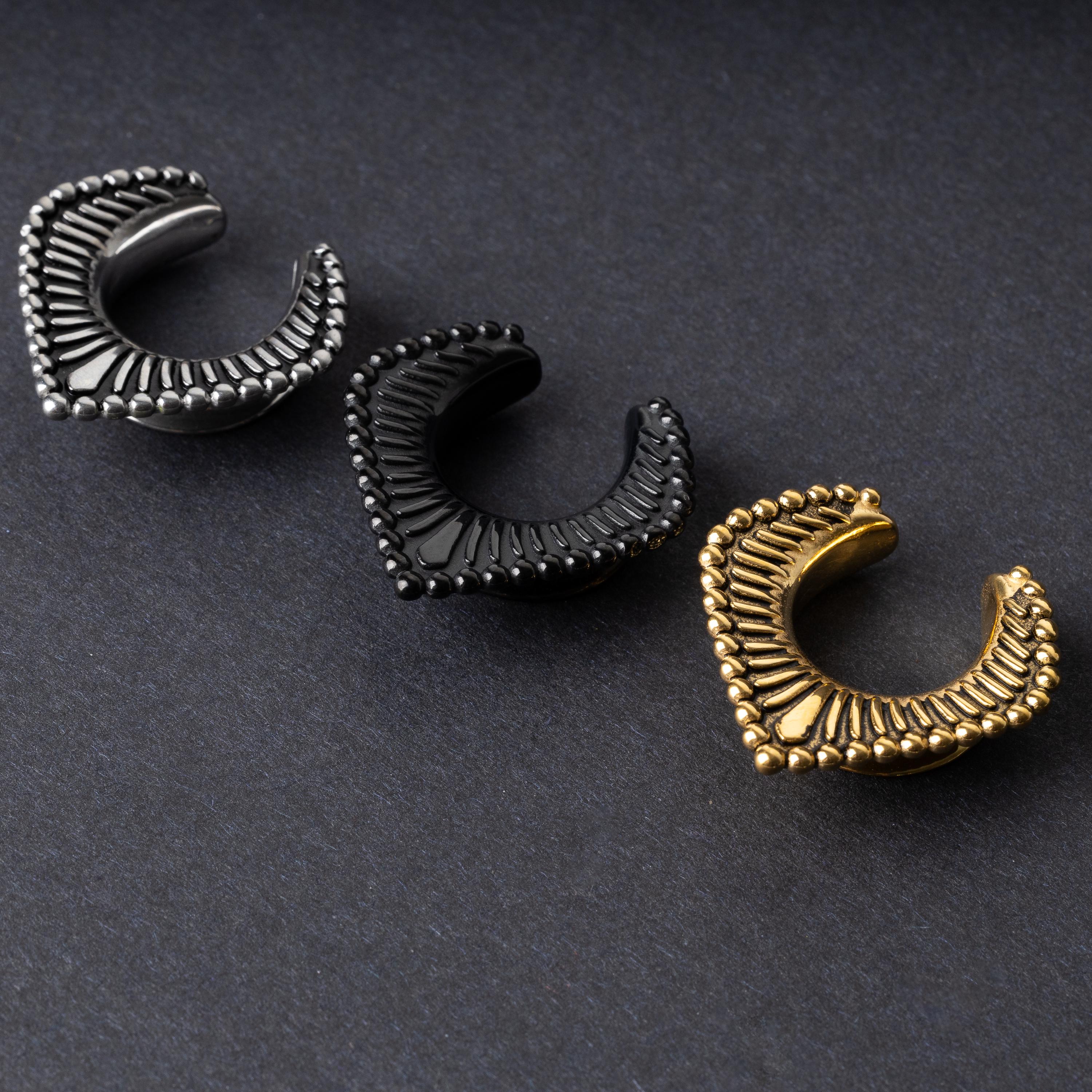 Three V-shaped stainless steel clickers in silver, black, and gold finishes arranged on a dark textured background.