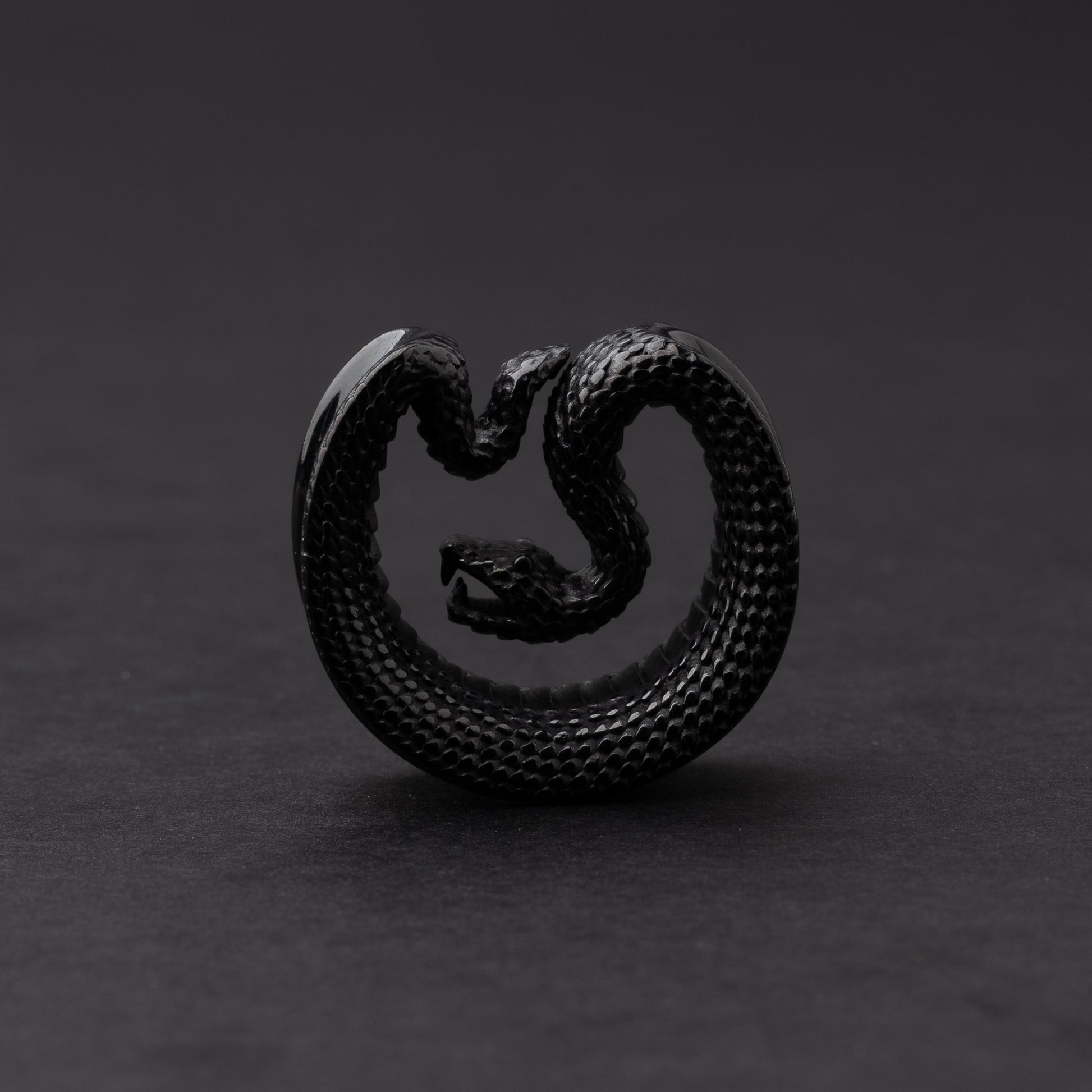 Black Snake-shaped saddle plugs, displayed on a dark background.