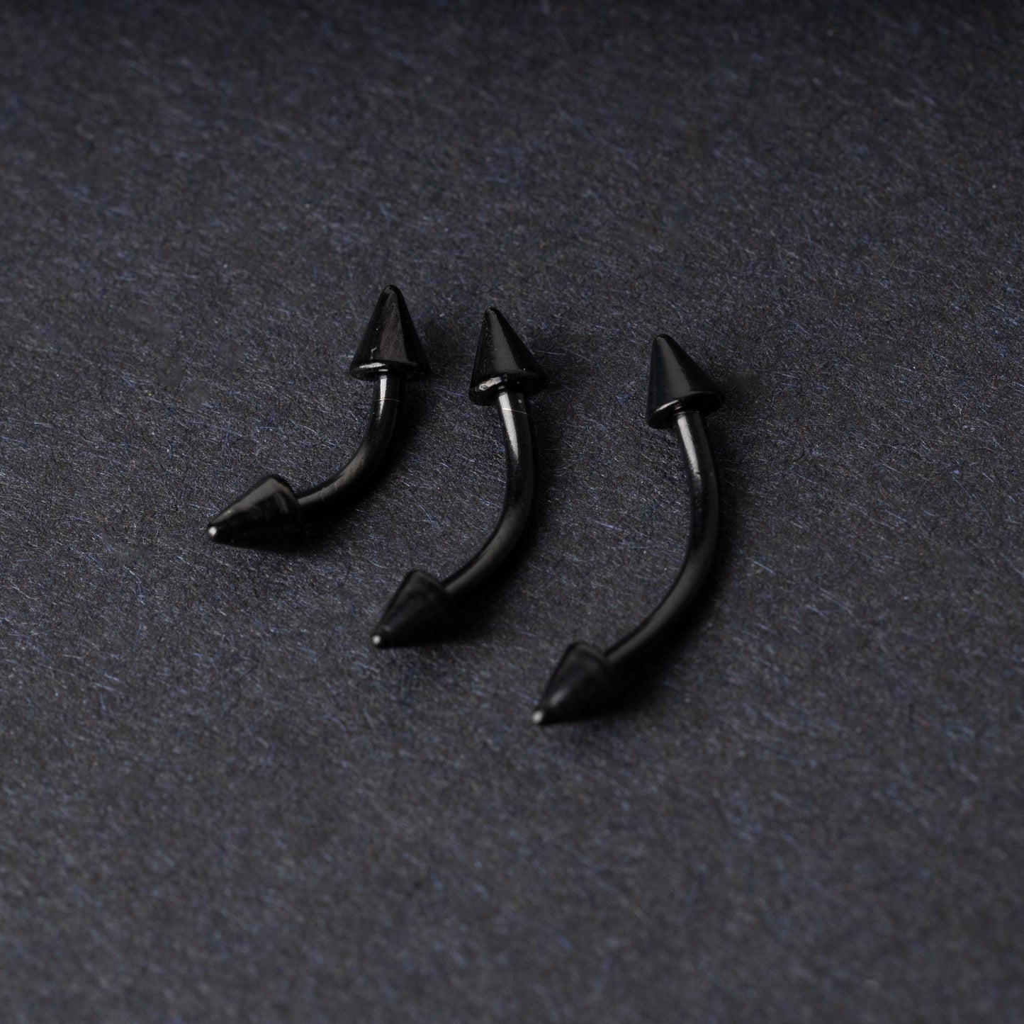 Three black curved barbells with spiked ends, displayed on a dark background with a polished finish.