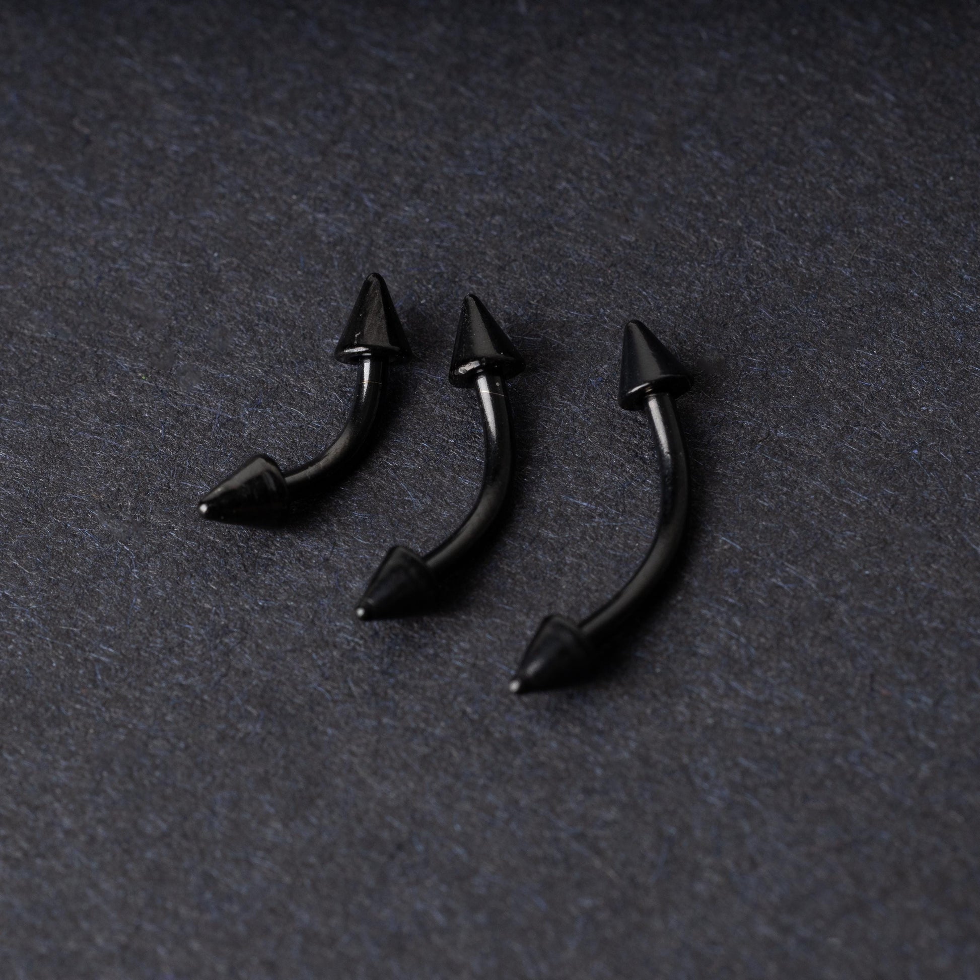 Three black curved barbells with spiked ends, displayed on a dark background with a polished finish.