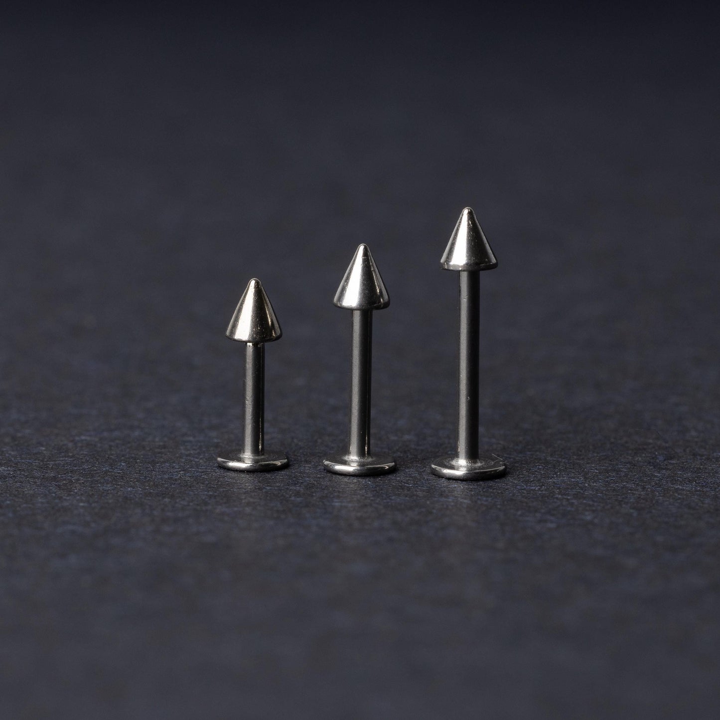 Three stainless steel flat-back barbells with spiked ends, displayed on a dark background showcasing their polished and sleek design.