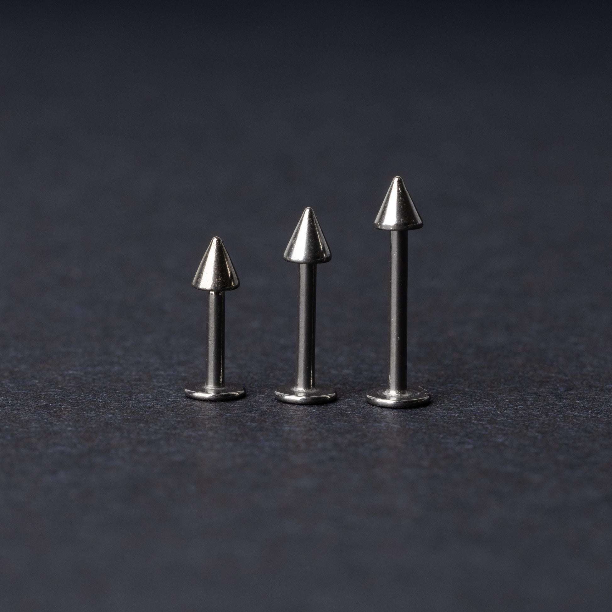 Three stainless steel flat-back barbells with spiked ends, displayed on a dark background showcasing their polished and sleek design.