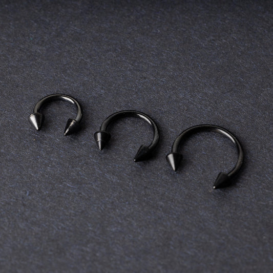 Three black stainless steel horseshoe rings with spiked ends in varying sizes, displayed on a dark background.