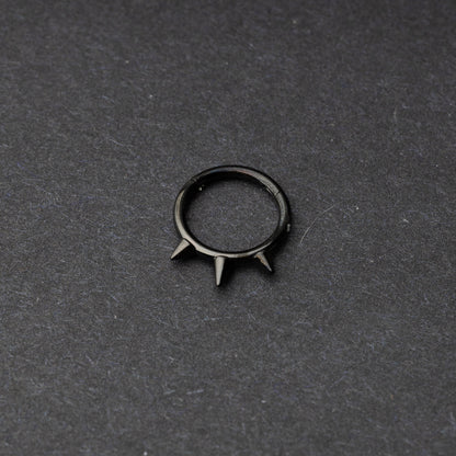 Black-tone stainless steel clicker ring with three spikes, displayed on a dark textured background.