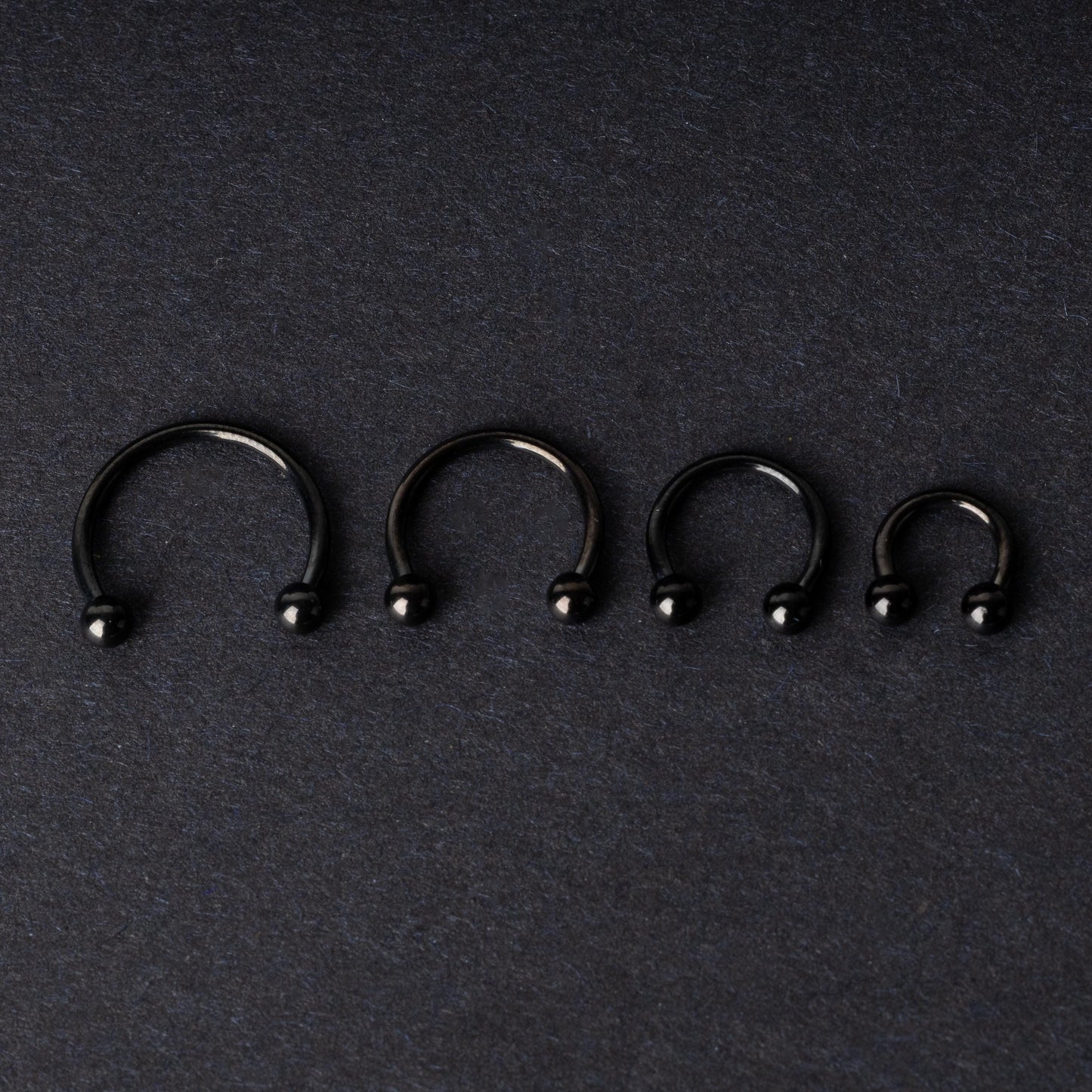 four G23 titanium black horseshoe rings with ball ends in varying sizes, displayed on a dark background showcasing their polished finish.