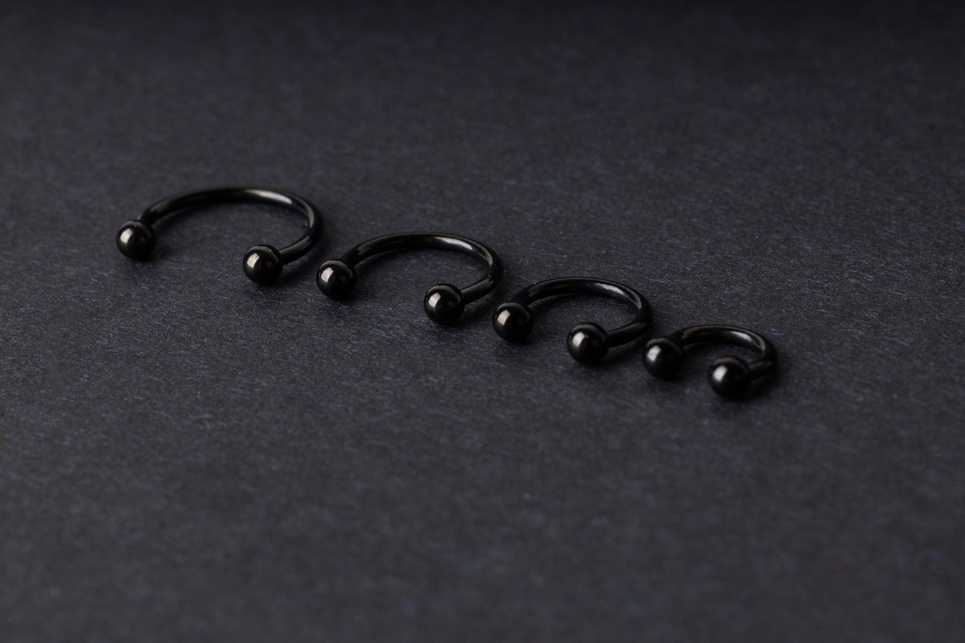 four G23 titanium black horseshoe rings with ball ends in varying sizes, displayed on a dark background showcasing their polished finish.