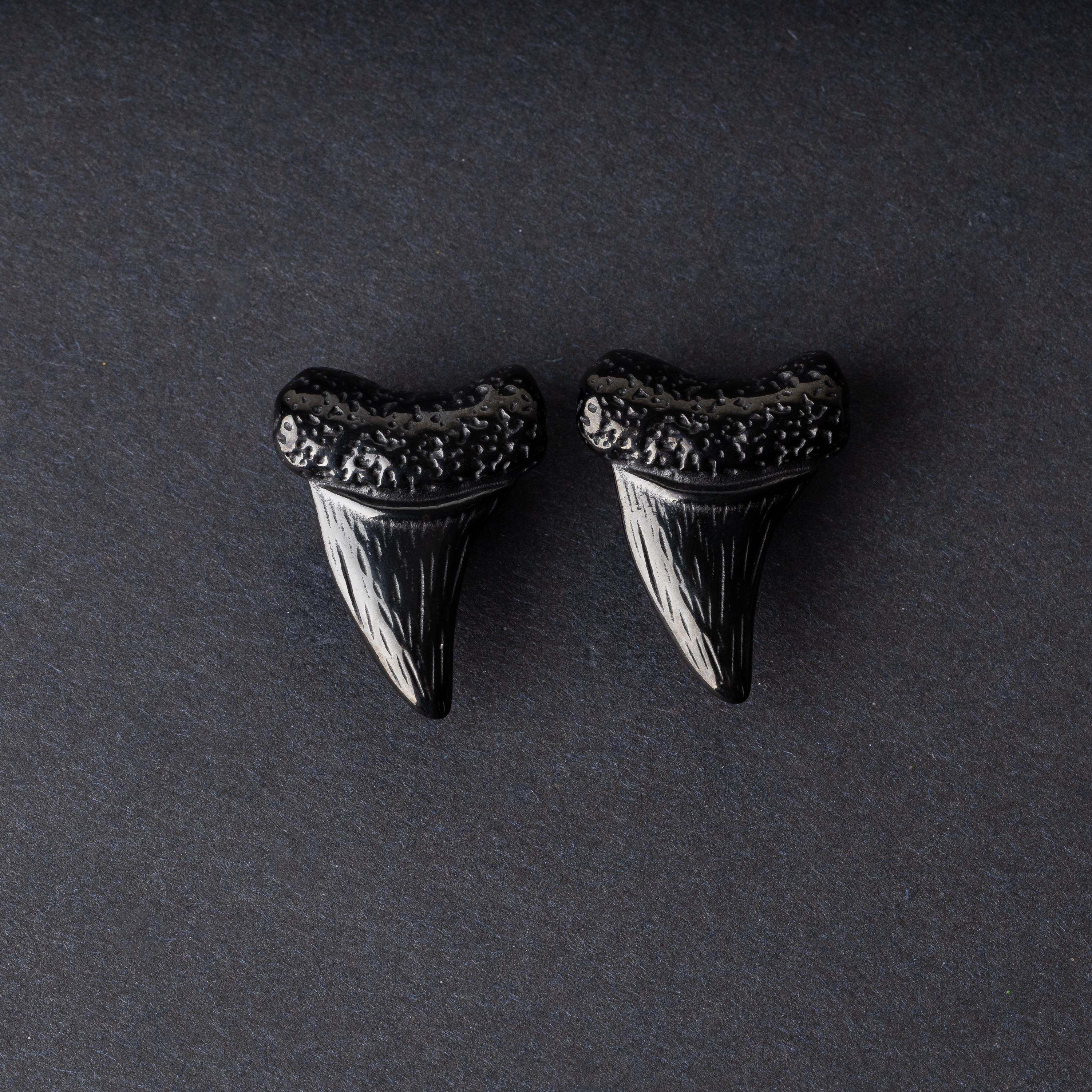 Close-up of black tooth ear weights featuring textured detailing, displayed on a dark background.

