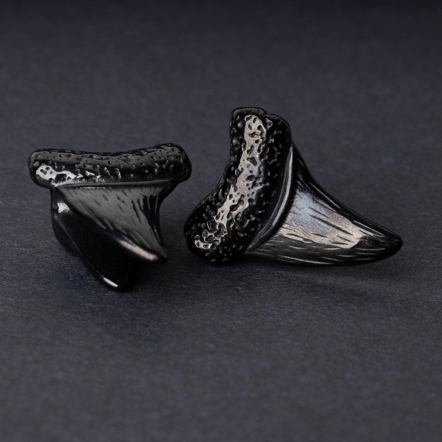 Close-up of black tooth ear weights featuring textured detailing, displayed on a dark background.

