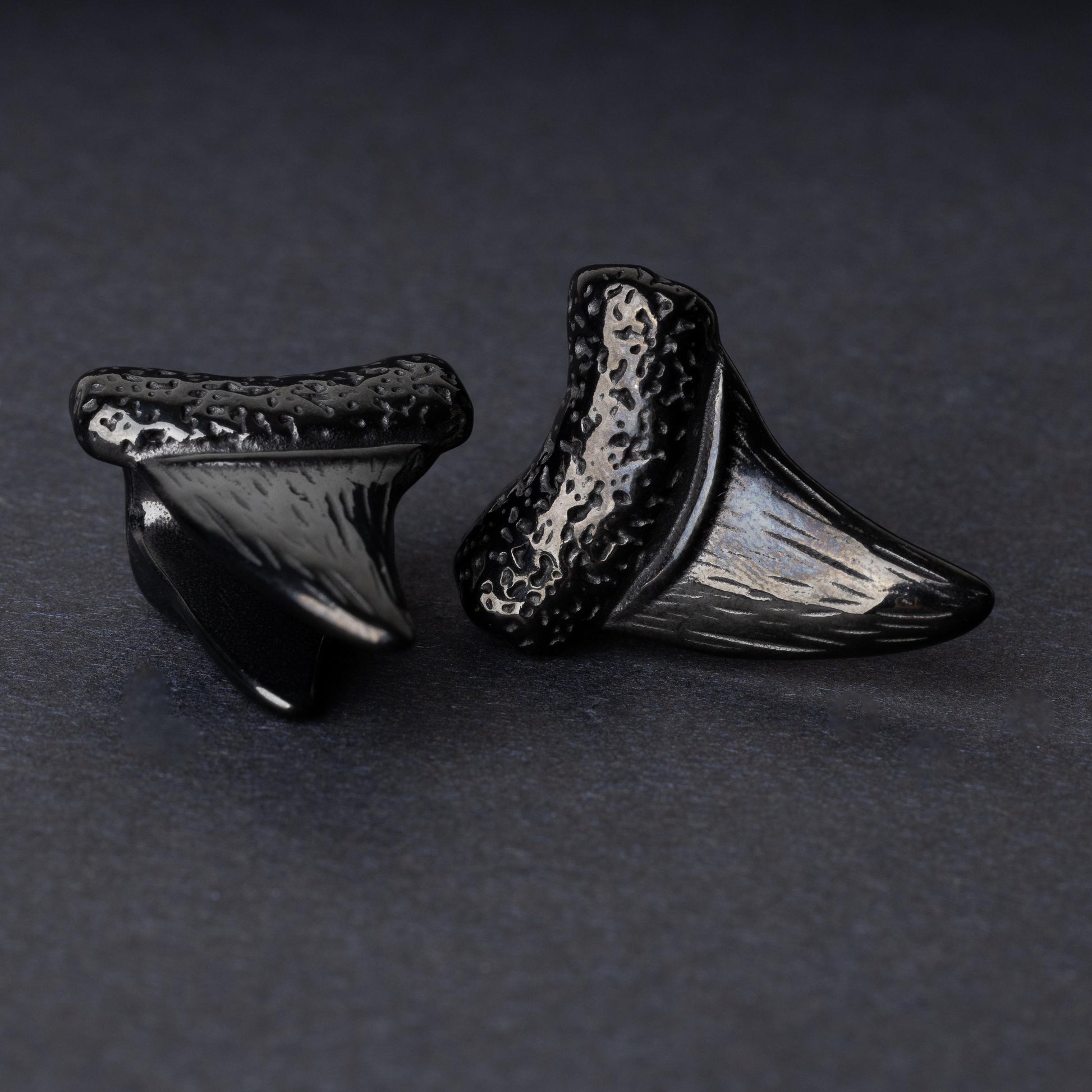 Close-up of black tooth ear weights featuring textured detailing, displayed on a dark background.

