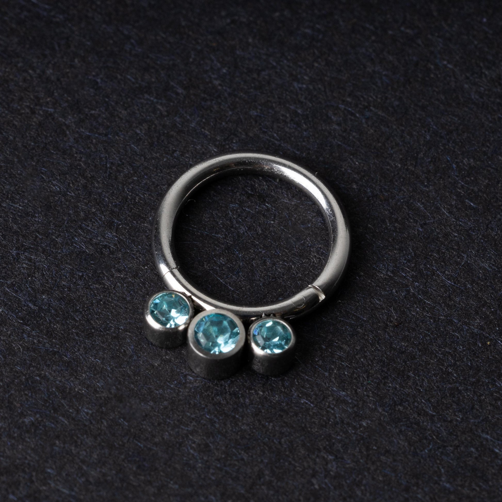 Titanium clicker ring with three aqua-blue gemstones, displayed on a dark background.
