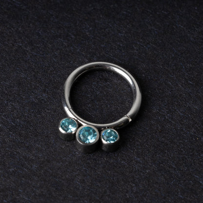 Titanium clicker ring with three aqua-blue gemstones, displayed on a dark background.