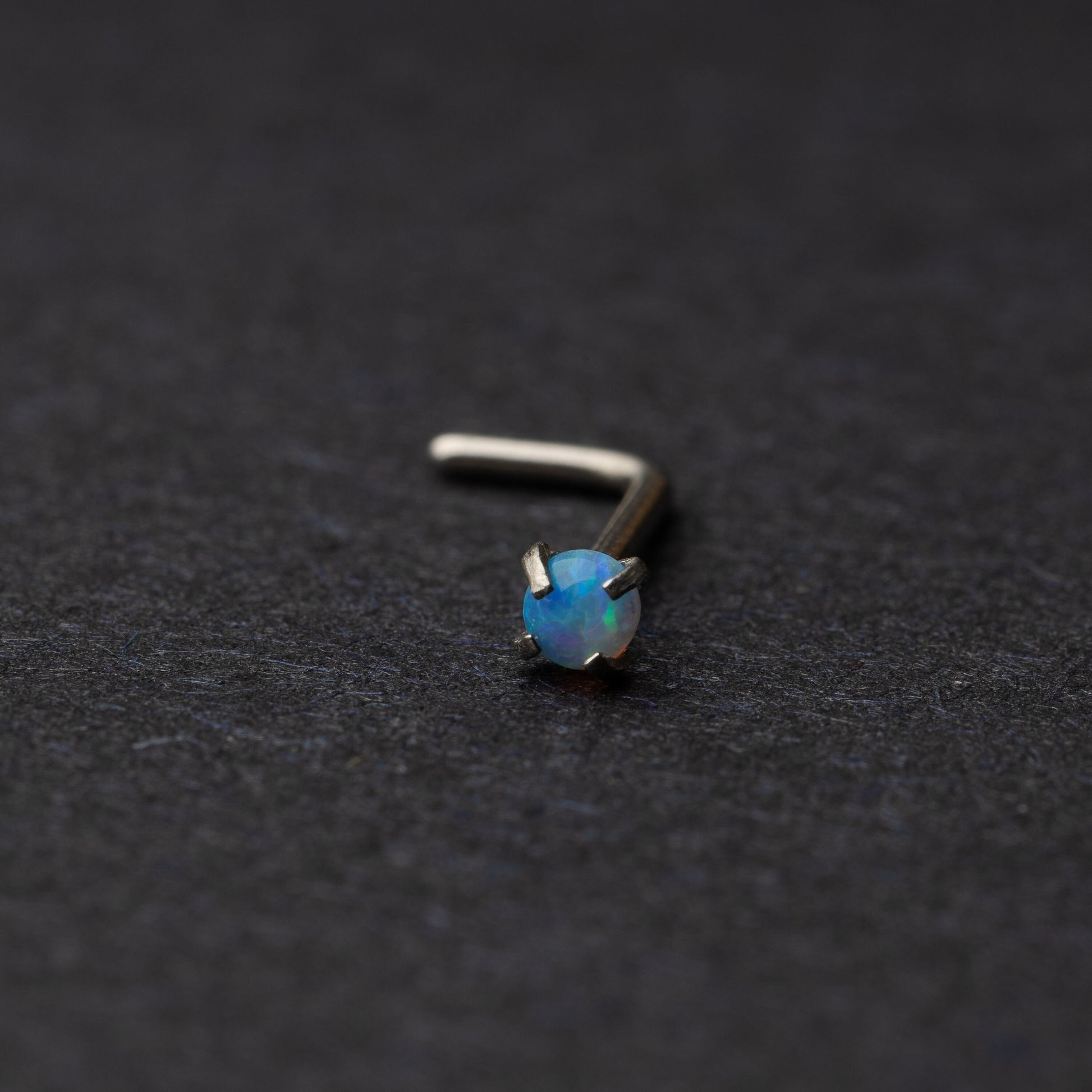 Opal L shaped nose stud on a dark background