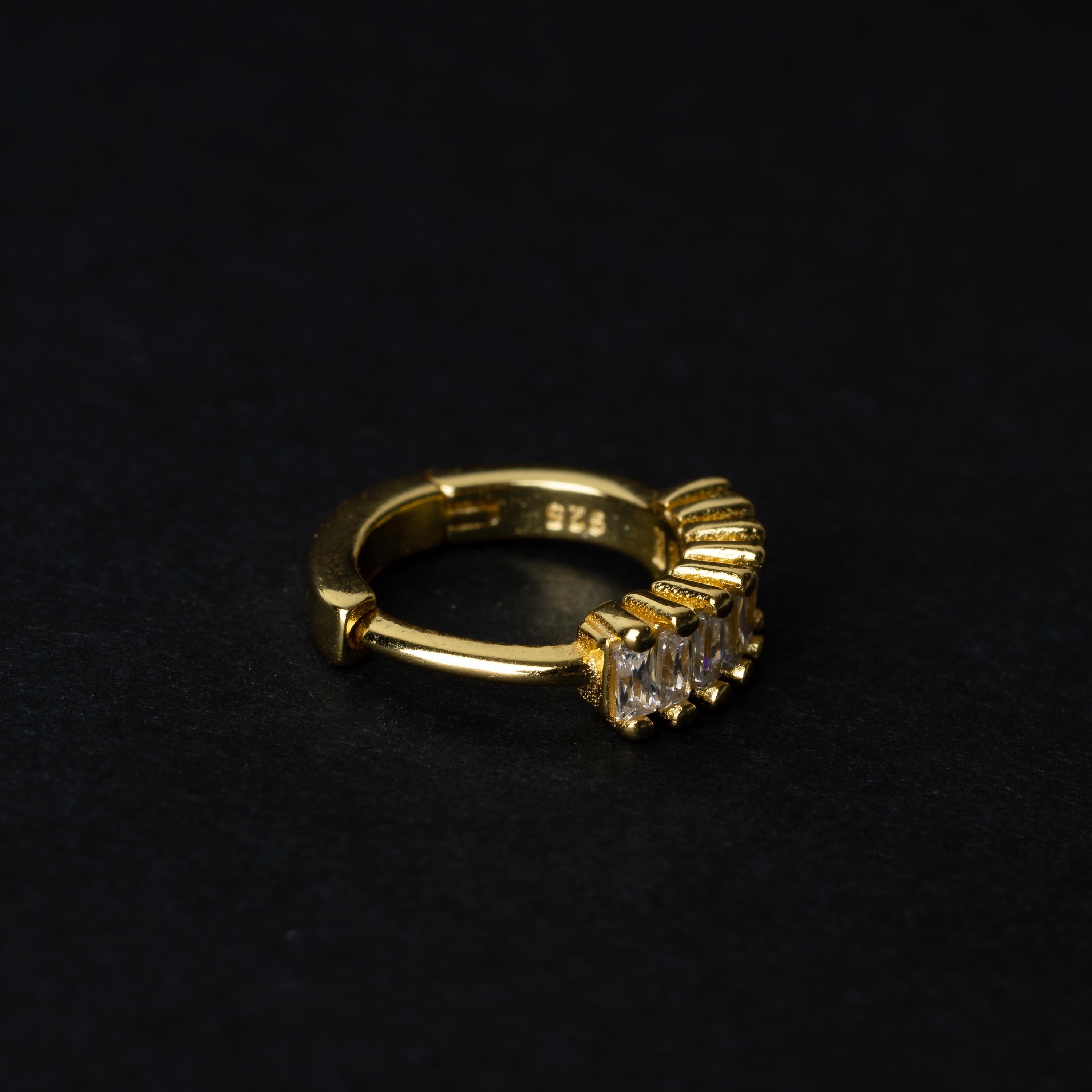 A gold septum clicker featuring a row of sparkling cubic zirconia gemstones, displayed on a black background.