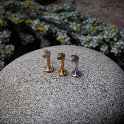 Gold, silver, and rose gold crescent moon labret studs displayed on a stone background