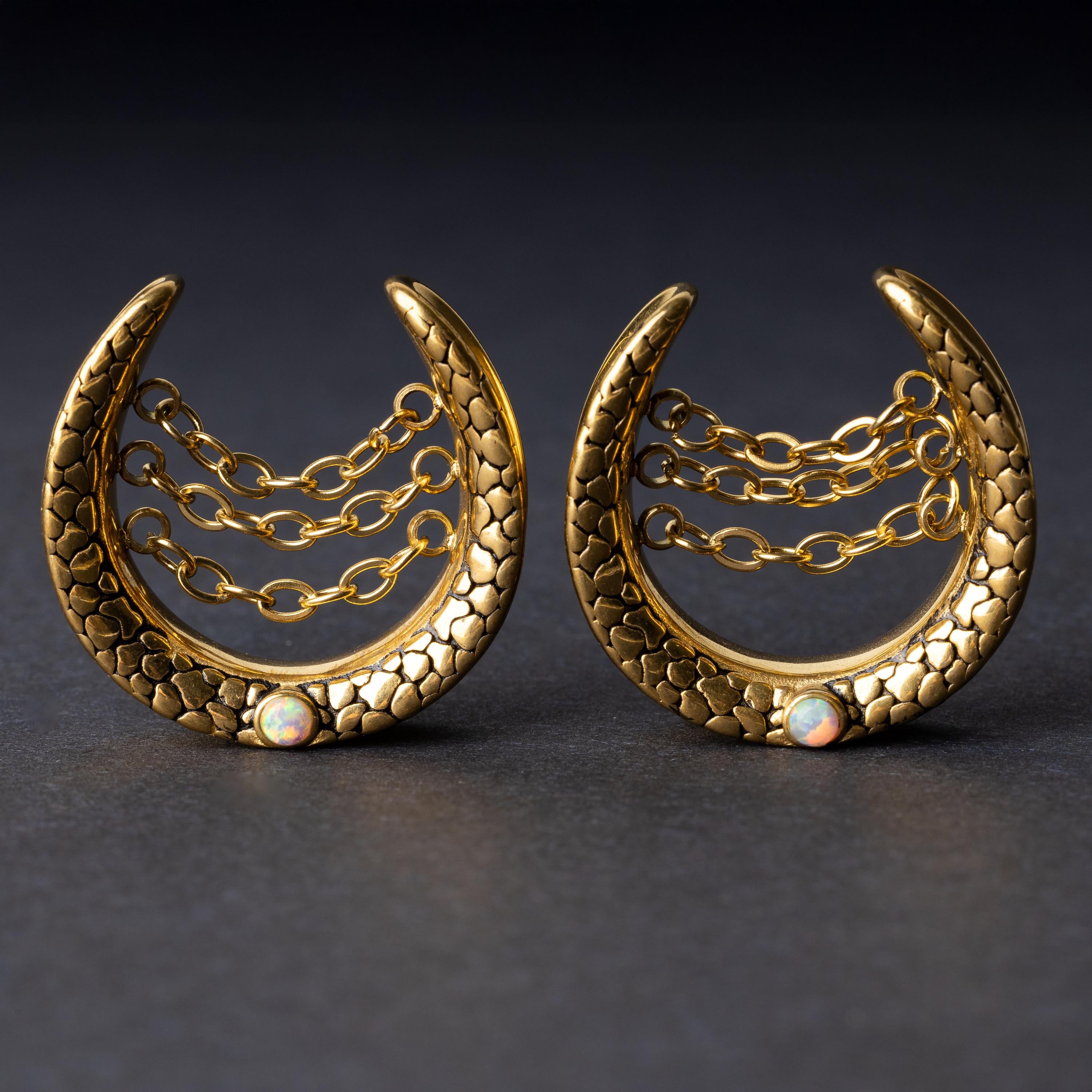 Pair of crescent-shaped hoops in gold with textured details, cascading chains, and an opal accent at the base, displayed on a dark background.