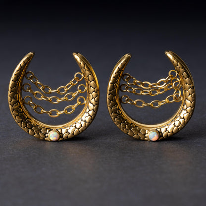 Pair of crescent-shaped hoops in gold with textured details, cascading chains, and an opal accent at the base, displayed on a dark background.