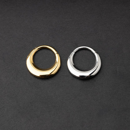 Crescent-shaped septum clickers, one in gold and one in silver, with a polished finish, displayed on a dark background.

