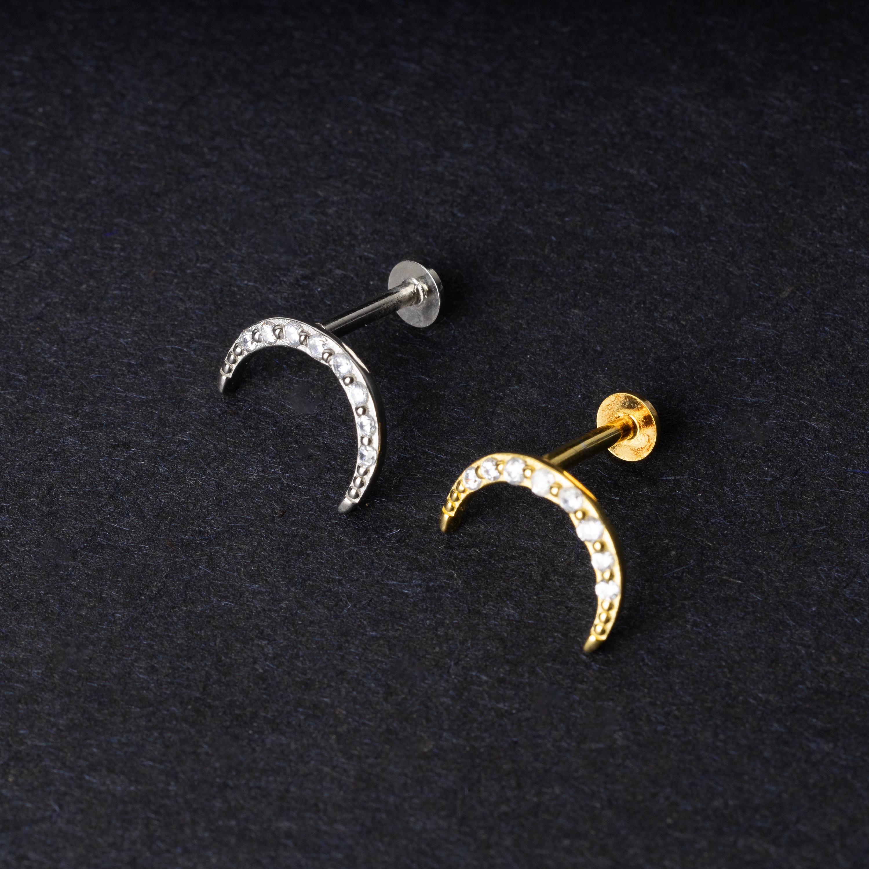 Close-up of gold and silver crescent moon stud earrings featuring CZ gems, displayed on a dark background.