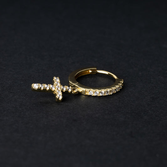 Gold hoop earring with cubic zirconia accents and a dangling cross charm, displayed on a dark background.