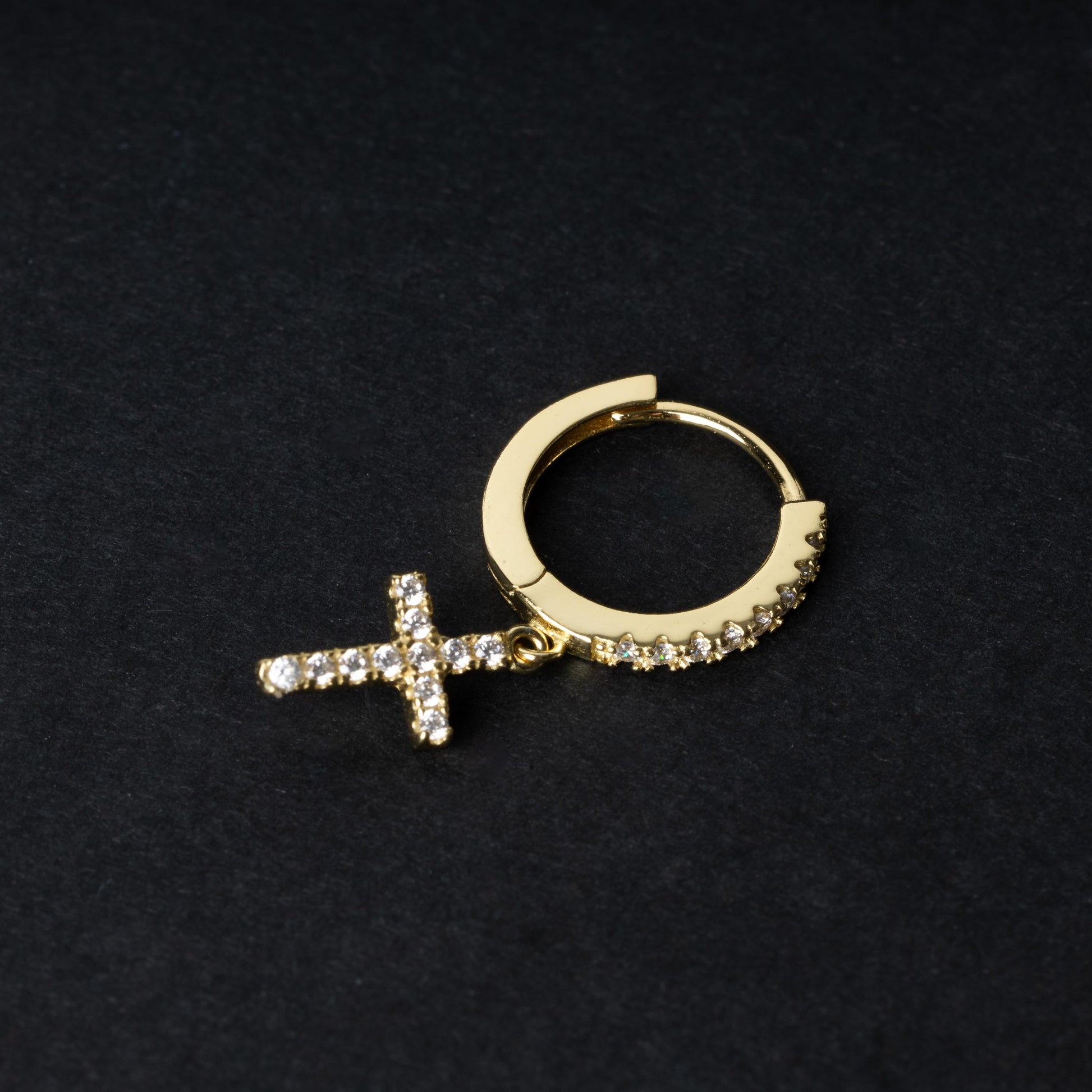 Gold hoop earring with cubic zirconia accents and a dangling cross charm, displayed on a dark background.
