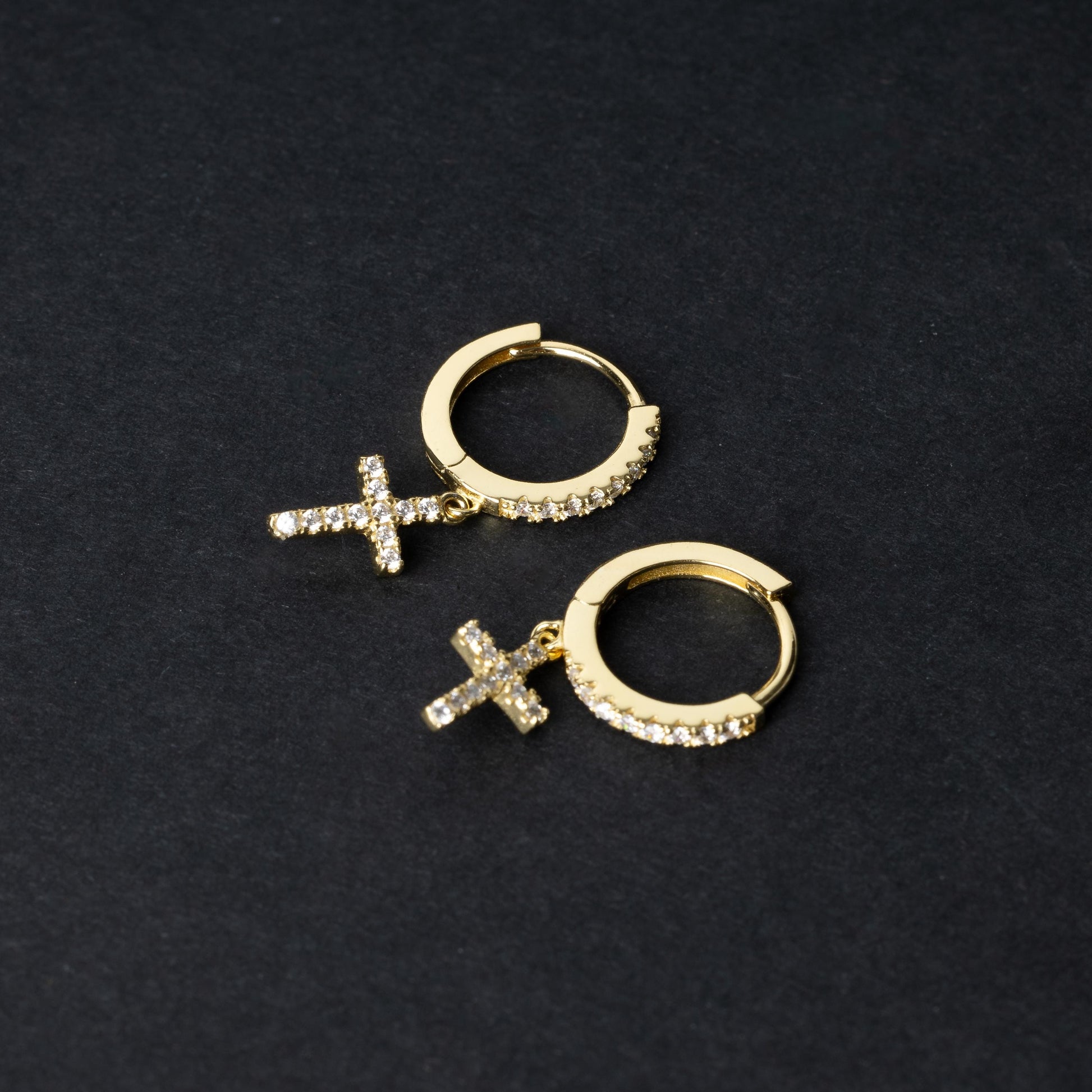 Gold hoop earrings with cubic zirconia accents and a dangling cross charm, displayed on a dark background.