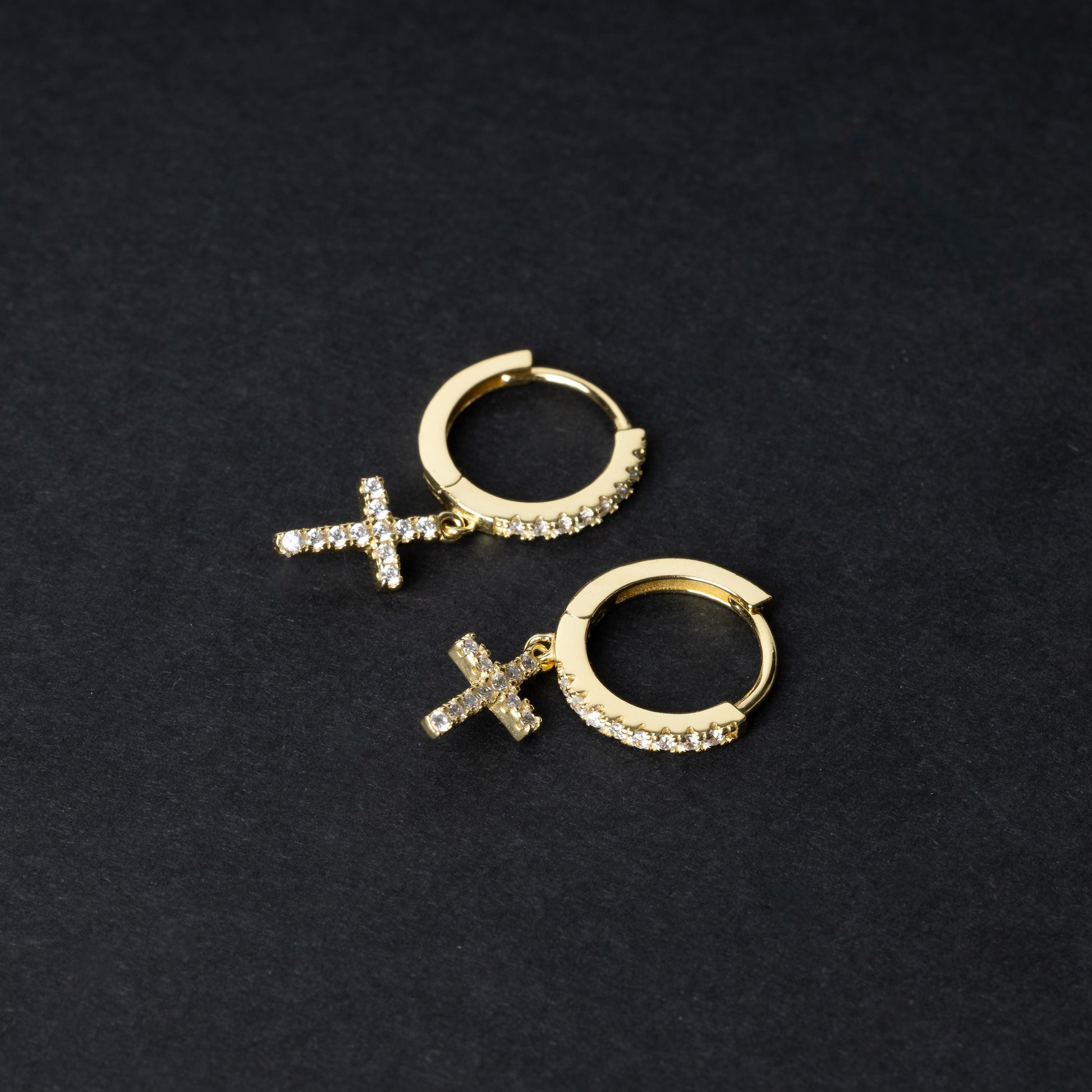 Gold hoop earrings with cubic zirconia accents and a dangling cross charm, displayed on a dark background.