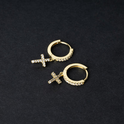Gold hoop earrings with cubic zirconia accents and a dangling cross charm, displayed on a dark background.