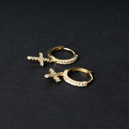 Gold hoop earrings with cubic zirconia accents and a dangling cross charm, displayed on a dark background.